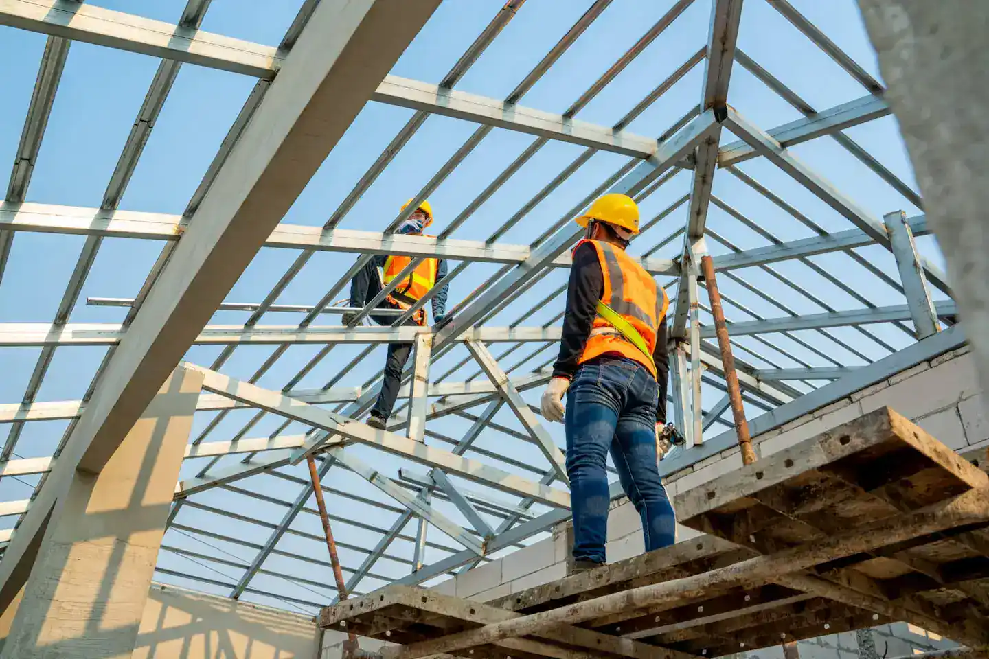 Construction workers wearing safety harnesses and high-visibility gear working on a residential roof frame, following working at heights requirements.