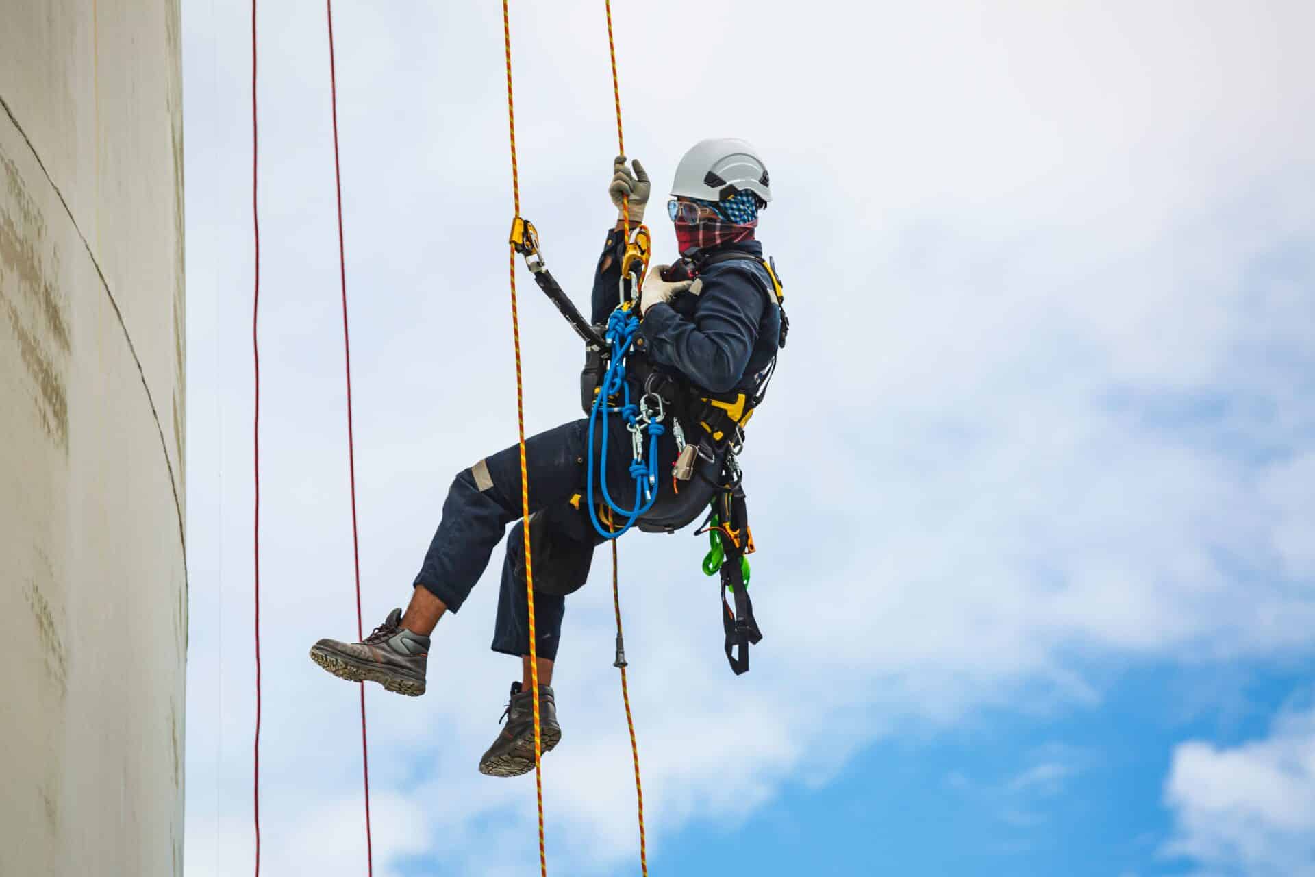A worker in full PPE performing a controlled descent from a tall structure against a blue sky, illustrating comprehensive working at heights course outcomes.
