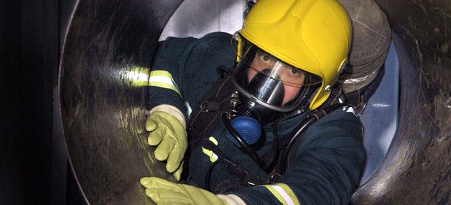 A person in a hard hat and protective gear is entering a circular confined space.